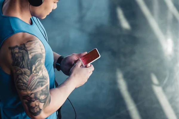 Jovem desportista usando smartphone com gráfico na tela e ouvir música — Fotografia de Stock