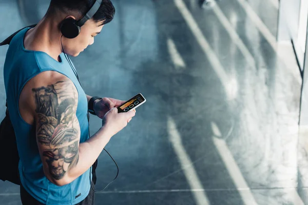 Joven deportista guapo usando el teléfono inteligente con gráfico en la pantalla y escuchando música - foto de stock