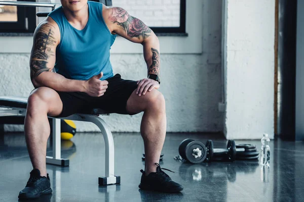 Cropped view of muscular young sportsman sitting at gym — Stock Photo