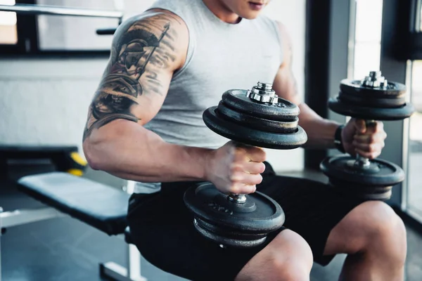 Vista parcial del joven deportista haciendo ejercicio con pesas en el gimnasio - foto de stock