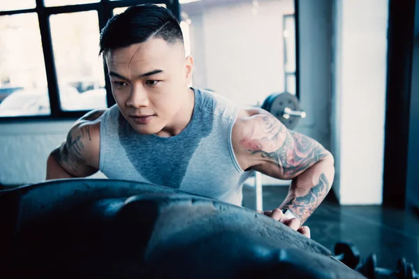 Nahaufnahme eines jungen asiatischen Sportlers, der im Fitnessstudio einen schweren Reifen umkippt — Stockfoto
