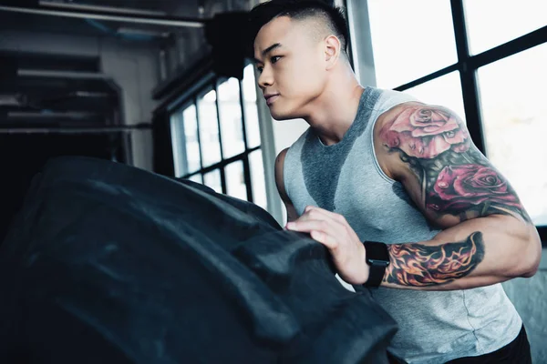 Young asian sportsman flipping heavy tire at gym — Stock Photo