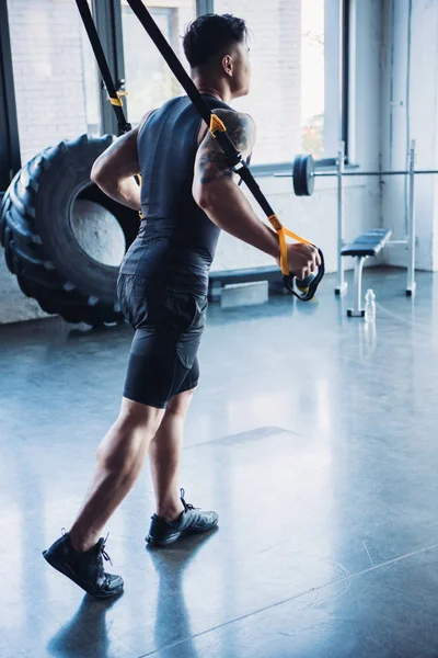 Side view of young muscular sportsman training with resistance bands in gym — Stock Photo