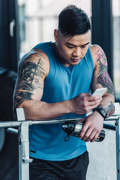 Schöner junger Sportler mit Smartphone im Fitnessstudio — Stockfoto