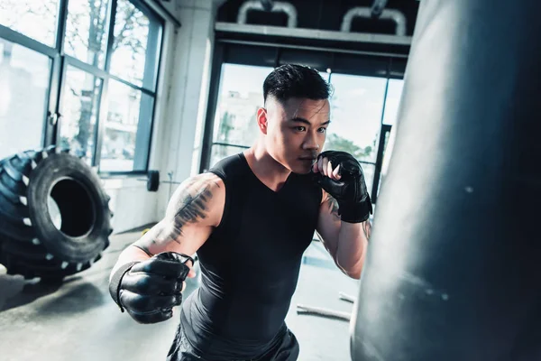 Молодой спортсмен в боксёрских перчатках и боксерской сумке в спортзале — стоковое фото