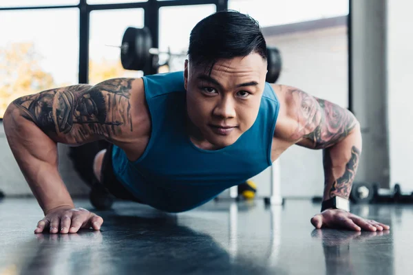 Сосредоточенный молодой азиатский спортсмен делает упражнения на доске в тренажерном зале — стоковое фото