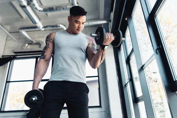 Concentrated young sportsman exercising with dumbbells in gym — Stock Photo