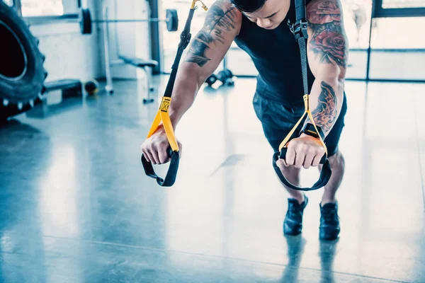 Cropped view of young muscular sportsman training with resistance bands in gym — Stock Photo