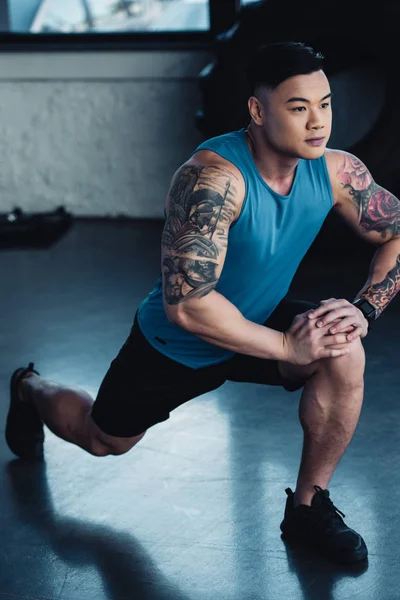 Enfocado joven asiático deportista haciendo embestida ejercicio en gimnasio - foto de stock