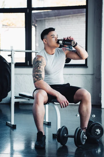 Young asian sportsman drinking water at gym — Stock Photo