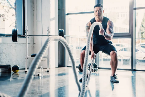 Joven deportista haciendo ejercicio con cuerdas de batalla en el gimnasio - foto de stock