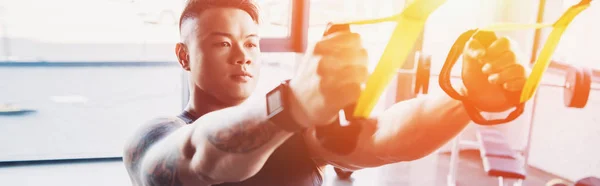 Young muscular asian sportsman training with resistance bands at gym in sunlight — Stock Photo