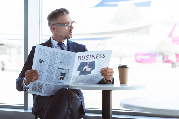 Homme d'affaires adulte lisant le journal et regardant la fenêtre à l'aéroport — Photo de stock