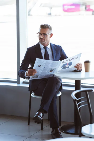 Erwachsener gutaussehender Geschäftsmann mit Brille liest Zeitung im Café am Flughafen — Stockfoto