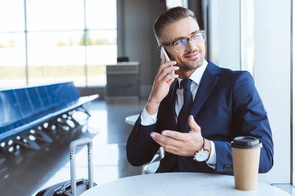 Adult businessman smiling and talking on smartphone at airport — Stock Photo