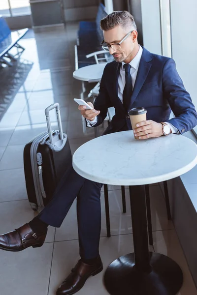 Erwachsener Geschäftsmann nutzt Smartphone und trinkt Kaffee am Flughafen — Stockfoto