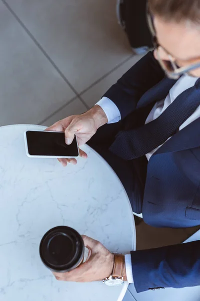 Hombre de negocios guapo en vasos con café para ir con teléfono inteligente en el aeropuerto - foto de stock