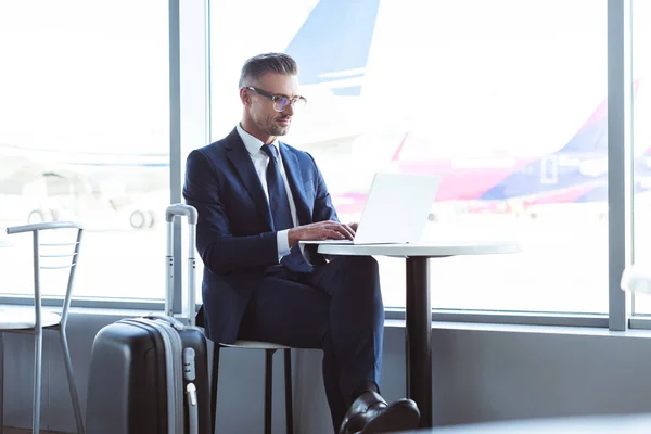 Hombre de negocios adulto en gafas de escribir en el ordenador portátil en el aeropuerto - foto de stock