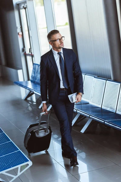 Homme d'affaires adulte en lunettes avec bagage marchant à l'aéroport — Photo de stock