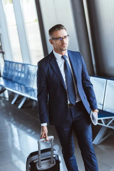Adulto guapo hombre de negocios en gafas con equipaje caminando en el aeropuerto - foto de stock