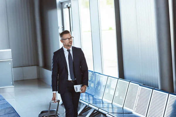 Adult handsome businessman in glasses with baggage and tickets walking at airport — Stock Photo