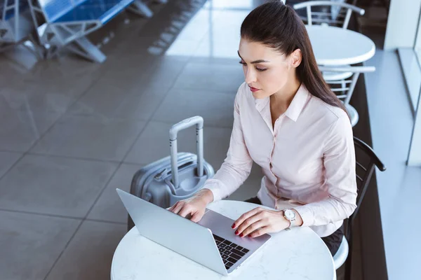 Young businesswoman with luggage using laptop at airport — Stock Photo