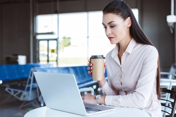 Jovem empresária com café para ir usando laptop no aeroporto — Fotografia de Stock