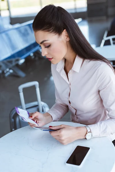 Junge Geschäftsfrau sitzt im Flughafencafé und hält Tickets — Stockfoto