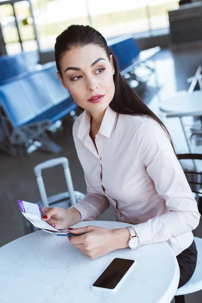 Junge Geschäftsfrau sitzt in Abflughalle und hält Tickets — Stockfoto