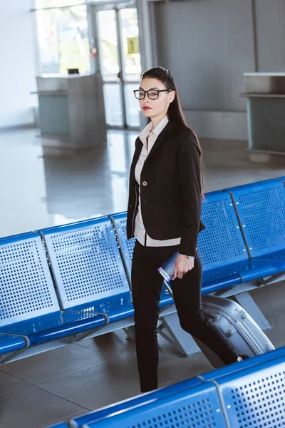 Jovem bela empresária em óculos andando com bagagem no aeroporto — Fotografia de Stock