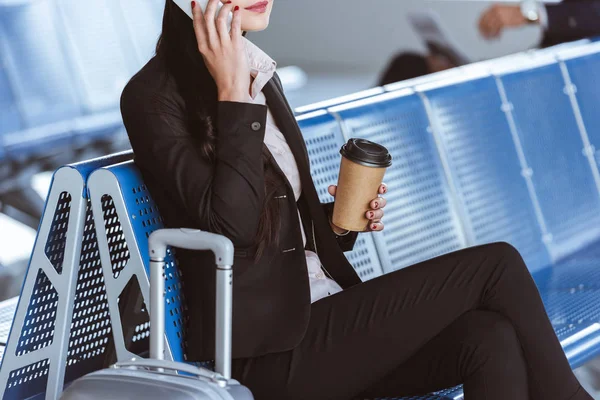 Крупним планом молода бізнес-леді в окулярах з багажем за допомогою смартфона в аеропорту — стокове фото