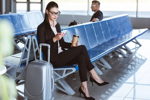 Jeune femme d'affaires en lunettes utilisant smartphone dans le salon de départ à l'aéroport — Photo de stock