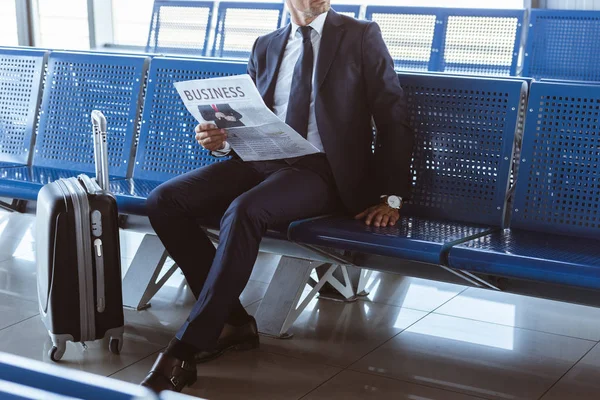 Primer plano del hombre de negocios adulto sentado en la sala de salida en el aeropuerto y leyendo el periódico - foto de stock
