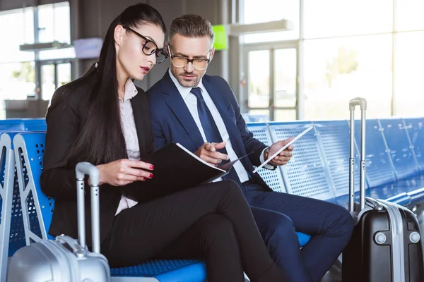 Дорослий бізнесмен використовує цифровий планшет, в той час як бізнес-леді тримає чорну теку в залі вильоту в аеропорту — стокове фото