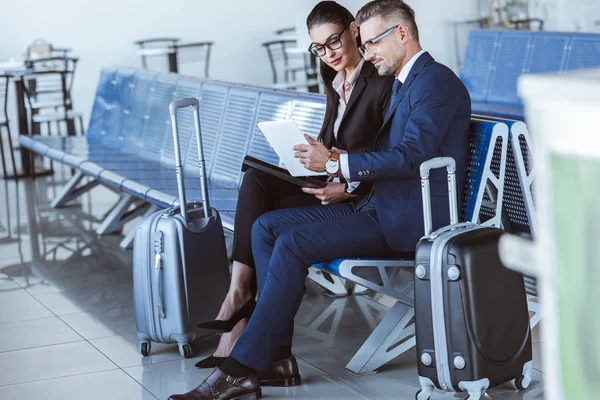 Adulto hombre de negocios y mujer de negocios sentado en la sala de salida y el uso de tabletas digitales en el aeropuerto - foto de stock