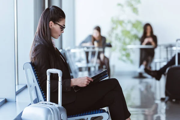 Adult businesswoman with black folder sitting at departure lounge in airport — Stock Photo