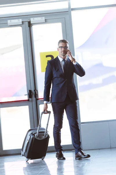 Erwachsener gutaussehender Geschäftsmann mit Brille und Smartphone am Flughafen — Stockfoto
