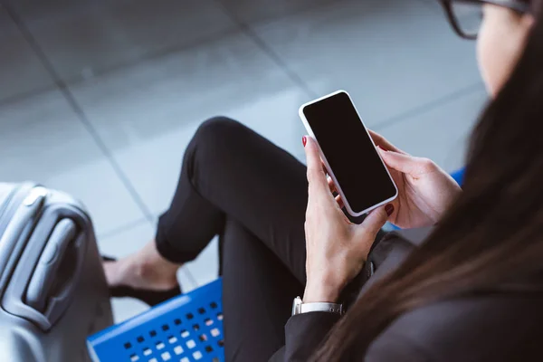 Junge Geschäftsfrau sitzt in Abflughalle am Flughafen und hält Smartphone in der Hand — Stockfoto