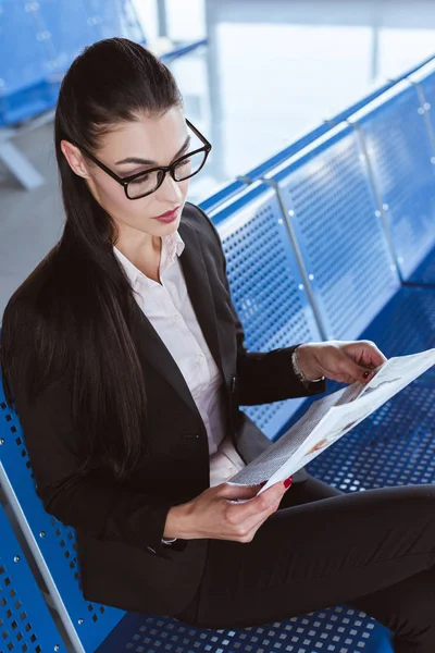 Young beautiful businesswoman in glasses reading newspaper at departure lounge in airport — Stock Photo