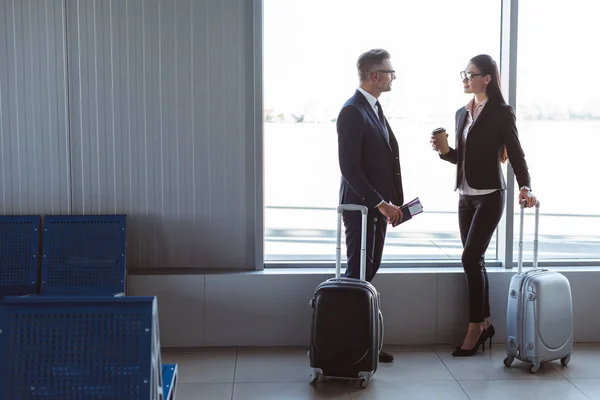 Hombre de negocios y mujer de negocios de pie y hablando en la sala de salida en el aeropuerto - foto de stock