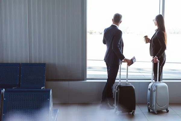 Бизнесмен и деловая женщина смотрят в окно в зале вылета в аэропорту — стоковое фото