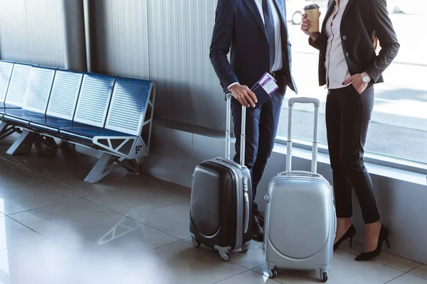 Бизнесмен с билетами и деловая женщина с кофе подойдут к окну в зале вылета в аэропорту — стоковое фото