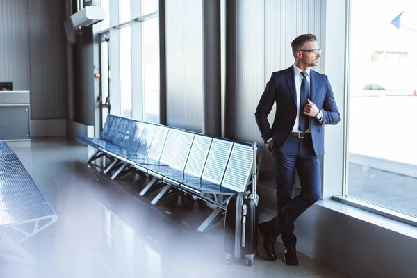 Красивый бизнесмен стоит в зале вылета и смотрит в окно в аэропорту — стоковое фото