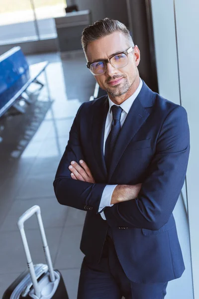 Hombre de negocios en gafas con los brazos cruzados de pie en la sala de salida en el aeropuerto - foto de stock