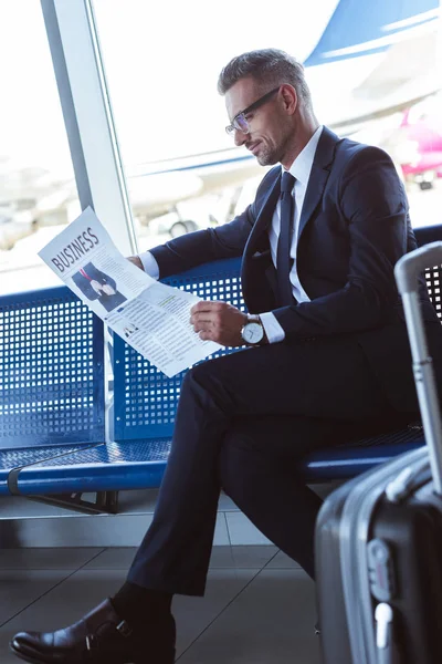 Hombre de negocios guapo sentado cerca de la ventana en la sala de salida y leer el periódico - foto de stock