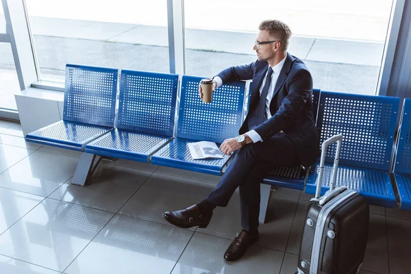 Empresário em óculos sentado com jornal e café para ir no aeroporto — Fotografia de Stock