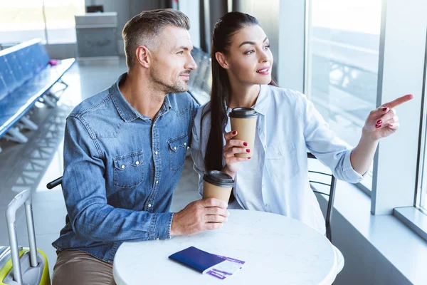 Pareja de adultos mirando a la ventana en la sala de salida en el aeropuerto - foto de stock