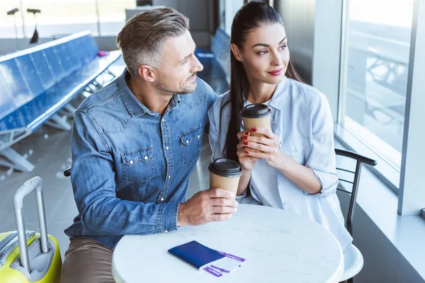 Couple adulte avec café pour aller regarder la fenêtre au salon de départ à l'aéroport — Photo de stock