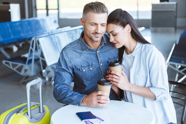 Casal adulto com café para ir abraçar no aeroporto — Fotografia de Stock