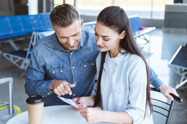 Romantische Paar wartet auf das Flugzeug am Flughafen, Mann zeigt etwas in das Ticket — Stockfoto